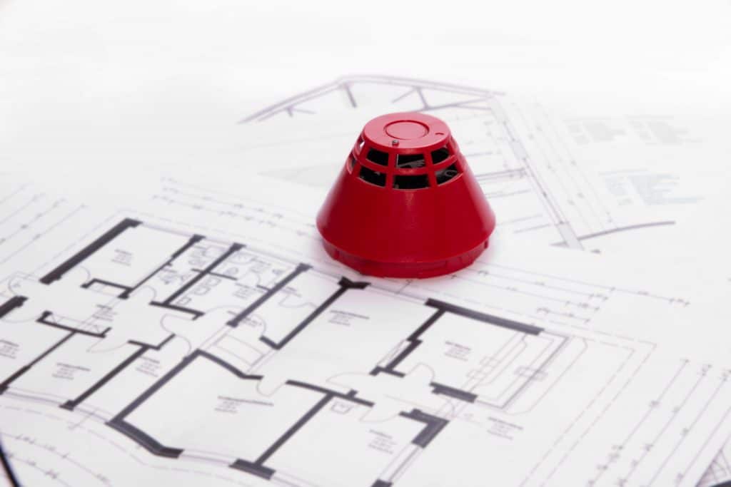 Fire saftey retrofit plans spread out on a table with a fire alarm sat on top