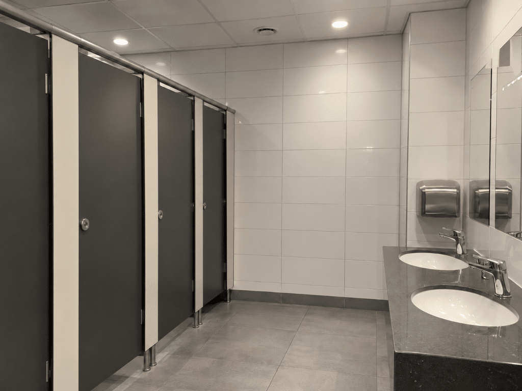 Modern workplace toilet with enclosed cubicles, tiled walls and handwashing facilities, highlighting the importance of ensuring fire alarms can be heard clearly in washroom areas.