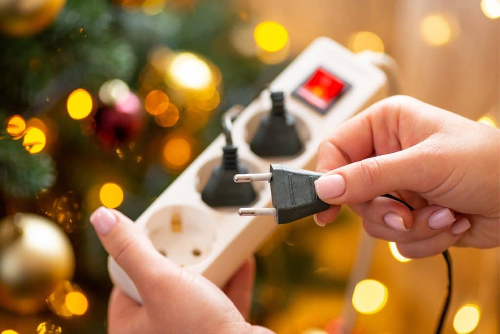 Close up of a woman hands plugging a plug in an electrical socket, close up.,Christmas tree on the background, electrical device at home